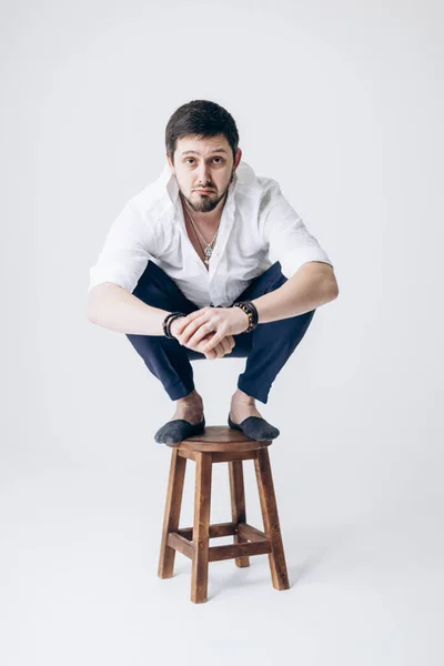 Portrait of handsome man with beard in white shirt sits on chair