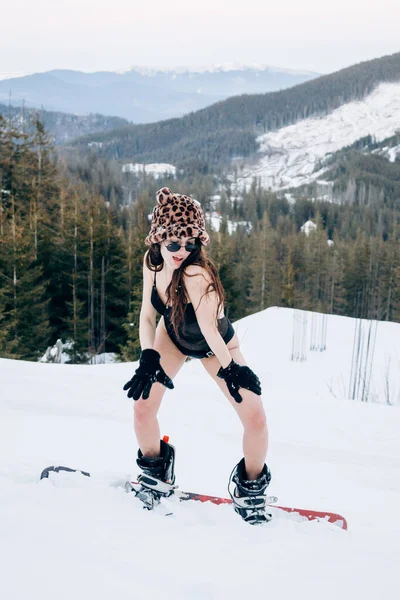 Piękna Dziewczyna Czarnym Body Stoi Snowboardzie Środku Zaśnieżonych Gór Drzew — Zdjęcie stockowe
