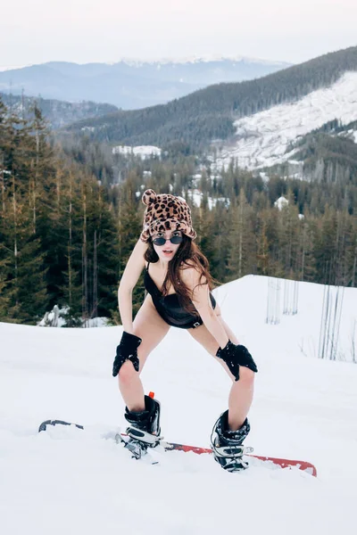 身穿黑色紧身衣的漂亮姑娘站在雪山森林中间的雪板上 — 图库照片