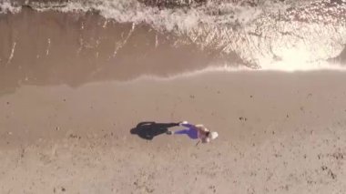 Yukarıdan drone görüntüsü. Kız yaz tatilinde ıslak kumsalda dalgalarla koşuyor.