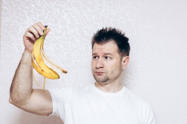 Beyaz tişörtlü adam elinde kayıp bir muz tutuyor. Ereksiyon sorunu, erkek sağlığı