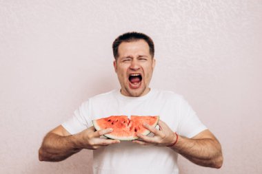 Beyaz tişörtlü adam olgun karpuz tutuyor ve yiyor. Bahçeden yaz meyveleri