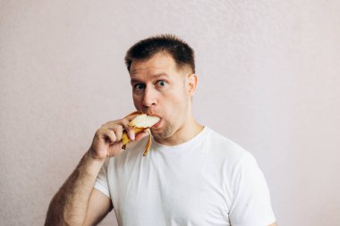 Beyaz tişörtlü adam olgun sarı muzu tutuyor ve yiyor. Bahçeden yaz vitamini meyveleri