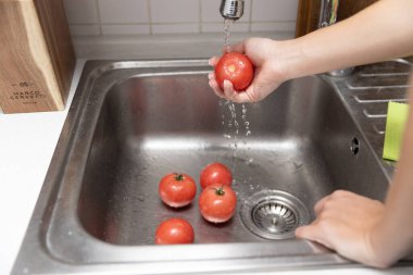 Kadınların elleri lavaboda kırmızı domatesleri yıkıyor. Mutfakta domates soyuyorlar.