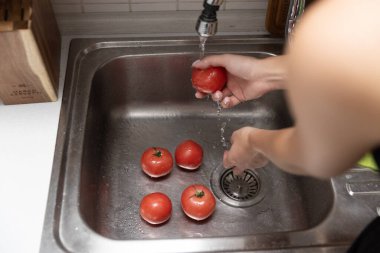 Kadınların elleri lavaboda kırmızı domatesleri yıkıyor. Mutfakta domates soyuyorlar.