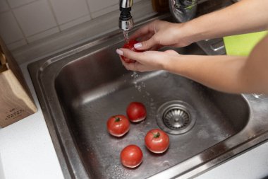 Kadınların elleri lavaboda kırmızı domatesleri yıkıyor. Mutfakta domates soyuyorlar.