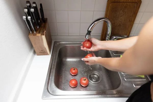 Women\'s hands wash red tomatoes in sink. Peeling tomatoes under water in kitchen
