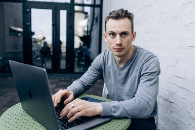 Gri ceketli adam, bilişim uzmanı, dizüstü bilgisayarda oturuyor ve çalışıyor.