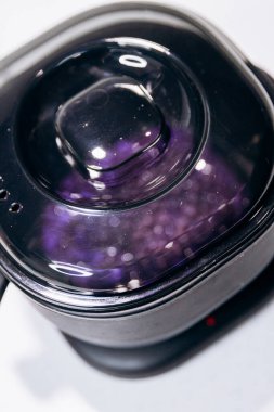 Purple granules are heated in black wax melter. Eyebrow tools clipart