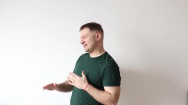 Yeşil tişörtlü adam beyaz arka planda dans ediyor.
