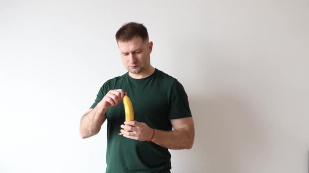 Mann Grünen Shirt Öffnet Banane Und Beginnt Sie Essen — Stockvideo