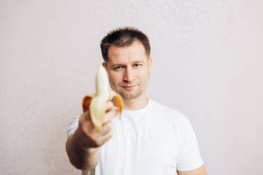 Beyaz tişörtlü adam kol mesafesinde açık bir muz tutuyor. Erkek sağlığı ve iktidarla ilgili sorunlar