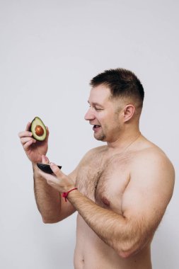 Tişörtsüz bir adam avacado tutar ve tatmin olur.