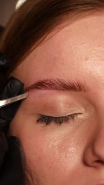 Makyöz işyeri aynanın önünde kaşlarını yapıyor.