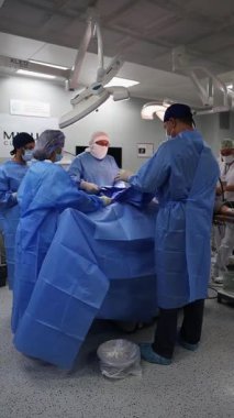 Deneyimli mavi önlüklü cerrahlar hastane ameliyathanesinde askeri bir hastayı ameliyat ederler.