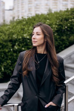 Çekici esmer, uzun kahverengi saçlı. Deri ceketli kameraya poz veriyor ve baharda açık havada kot pantolon giyiyor.