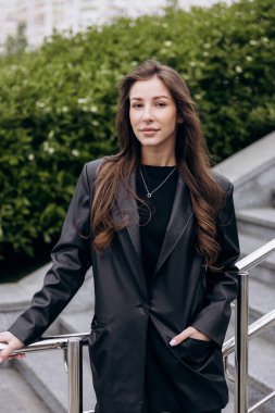 Çekici esmer, uzun kahverengi saçlı. Deri ceketli kameraya poz veriyor ve baharda açık havada kot pantolon giyiyor.