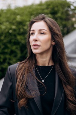 Çekici esmer, uzun kahverengi saçlı. Deri ceketli kameraya poz veriyor ve baharda açık havada kot pantolon giyiyor.