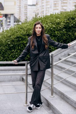 Çekici esmer, uzun kahverengi saçlı. Deri ceketli kameraya poz veriyor ve baharda açık havada kot pantolon giyiyor.