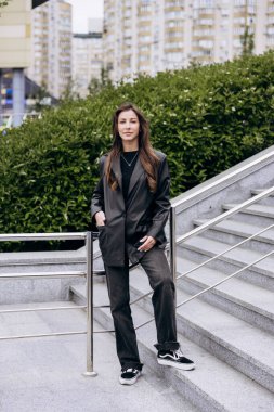 Çekici esmer, uzun kahverengi saçlı. Deri ceketli kameraya poz veriyor ve baharda açık havada kot pantolon giyiyor.