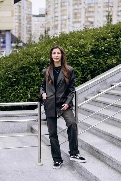 Çekici esmer, uzun kahverengi saçlı. Deri ceketli kameraya poz veriyor ve baharda açık havada kot pantolon giyiyor.