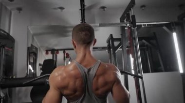 pumped-up man is training in a gym. Bodybuilder pumping with dumbbells, exercise machines, barbell