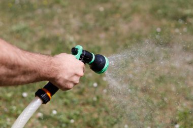 Adamın eli hortumu tutuyor ve bahçeye su serpiyor.