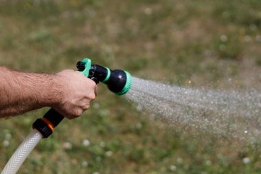 Adamın eli hortumu tutuyor ve bahçeye su serpiyor.