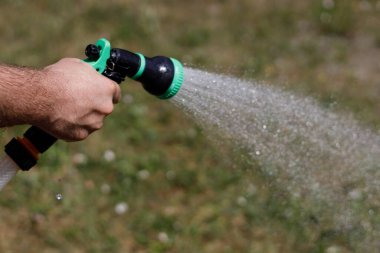 Adamın eli hortumu tutuyor ve bahçeye su serpiyor.