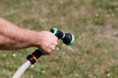 Adamın eli hortumu tutuyor ve bahçeye su serpiyor.