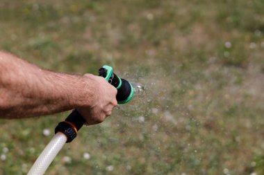 Adamın eli hortumu tutuyor ve bahçeye su serpiyor.