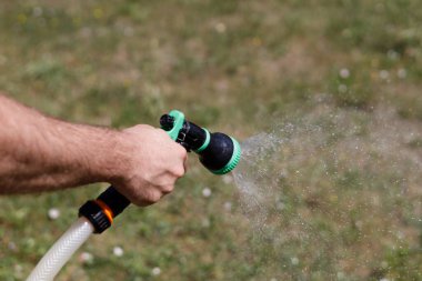 Adamın eli hortumu tutuyor ve bahçeye su serpiyor.