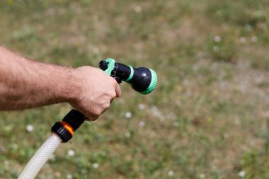 Adamın eli hortumu tutuyor ve bahçeye su serpiyor.