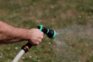 Adamın eli hortumu tutuyor ve bahçeye su serpiyor.