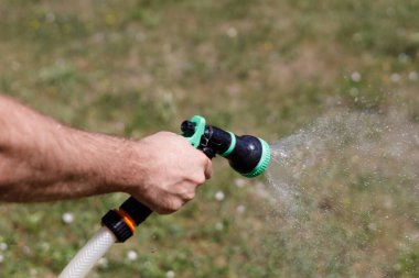 Adamın eli hortumu tutuyor ve bahçeye su serpiyor.