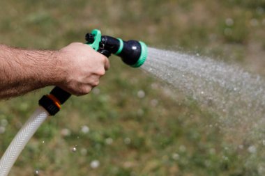 Adamın eli hortumu tutuyor ve bahçeye su serpiyor.