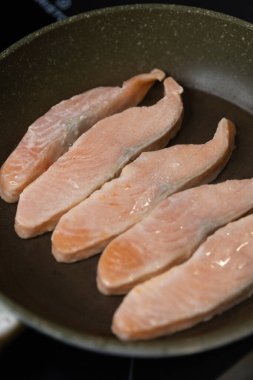 Bifteğe kesilmiş çiğ somon kızartma tavasında yatıyor ve kızartılıyor.