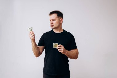 Siyah tişörtlü adam elinde prezervatif tutuyor..