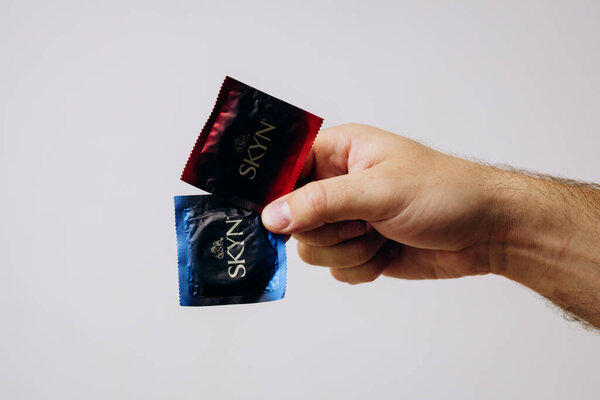 Мужская рука держит презервативы на белом фоне