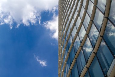 Curved glass skyscraper reflecting blue sky and white clouds. clipart