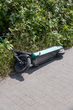Terk edilmiş bir e-scooter kaldırım kenarında çimlerde yatıyor. Yüksek kalite fotoğraf