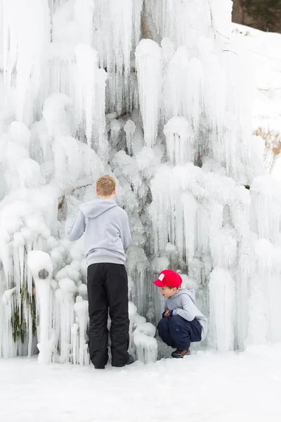 若い男の子が一緒に屋外で遊ぶ 冬の時間で凍った滝の隣に ストック写真