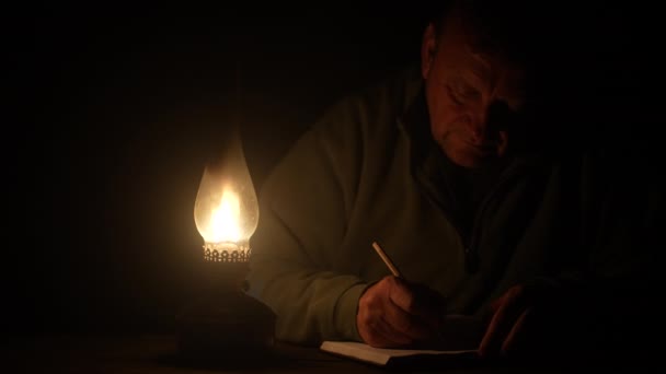 Mężczyzna Pisze Ołówkiem Notatniku Przy Świetle Lampy Naftowej Noc Zbliżenie — Wideo stockowe