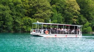 Plitvice Gölleri, Hırvatistan - 30 Ağustos 2021: İnsanlar yaz aylarında Hırvatistan, Orta Avrupa, seyahat ve doğa kavramları ile Plitvice Gölleri kıyıları boyunca turistik bir tekneye biniyor