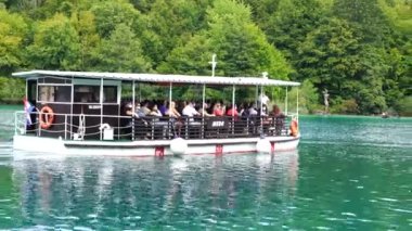 Plitvice Gölleri, Hırvatistan - 30 Ağustos 2021: İnsanlar yaz aylarında Hırvatistan, Orta Avrupa, seyahat ve doğa kavramları ile Plitvice Gölleri kıyıları boyunca turistik bir tekneye biniyor