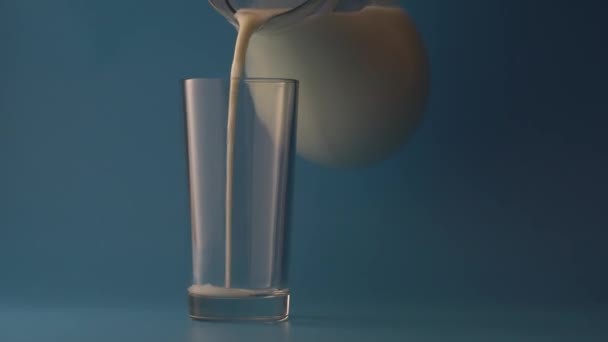 Γάλα Χύνεται Από Μια Κανάτα Ένα Άδειο Ποτήρι Μπλε Φόντο — Αρχείο Βίντεο