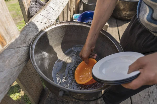 Ukrainian male farmer washes dishes with clean water in the farm yard , close up, outdoors. Rural traditions. West Ukraine