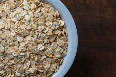 Tahta bir arka planda beyaz bir tabakta kuru yulaf ezmesi. Yulaf ezmesi yığını, üst görünüm, kapat, metin için boşluk kopyala