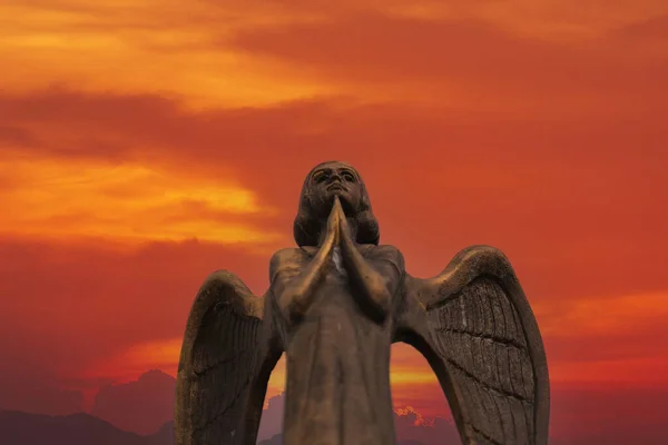 Detail of beautiful bronze statue of an angel with wings against the red sky. Beautiful angel with a red sky background with space for text, close up