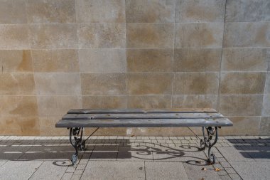 Bej renkli mermer duvara dayanan boş metal ahşap bir bank. Bir bank ve taş duvar arkaplanı, kapatın, boşluğu kopyalayın